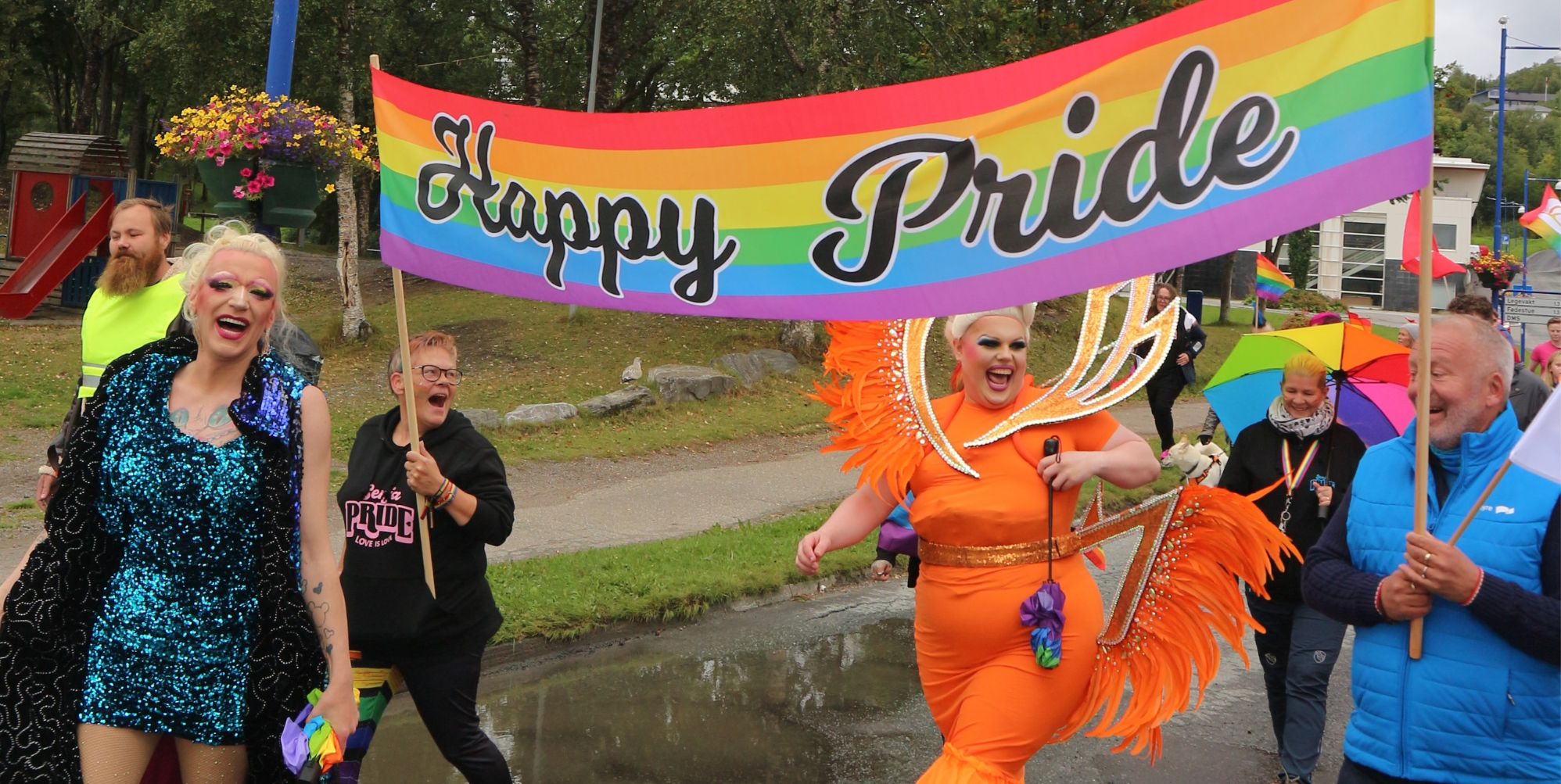 A photo from Senja Pride featuring smiling participants and drag queens holding a banner that says Happy Pride.