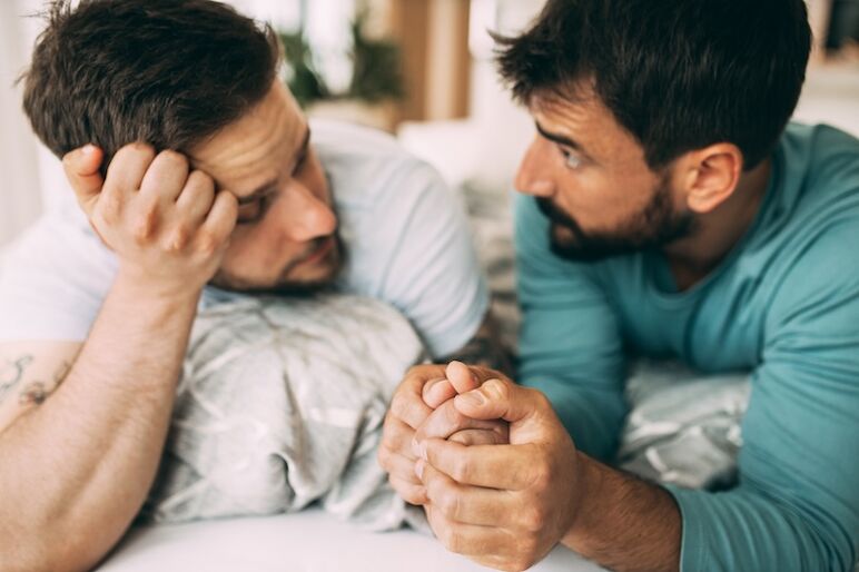 Pareja gay acostada en la cama, tomados de la mano y trabajando en su relación. Se cometen errores, no hay razón para repetirlos.