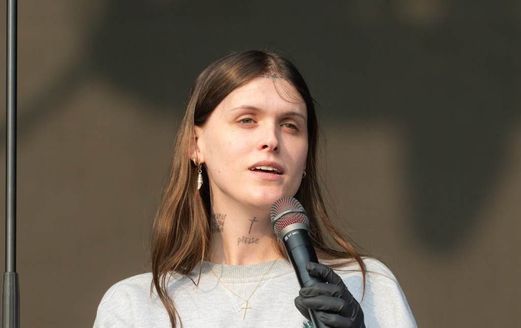 Ethel Cain actúa durante todos los puntos del Festival East. Ella sostiene el micrófono, vistiendo una sudadera gris con un collar cruzado de oro.