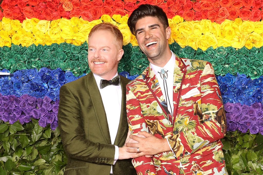 La familia moderna Jesse Tyler Ferguson y su esposo Justin Mikita frente a una pared de flores del arco iris