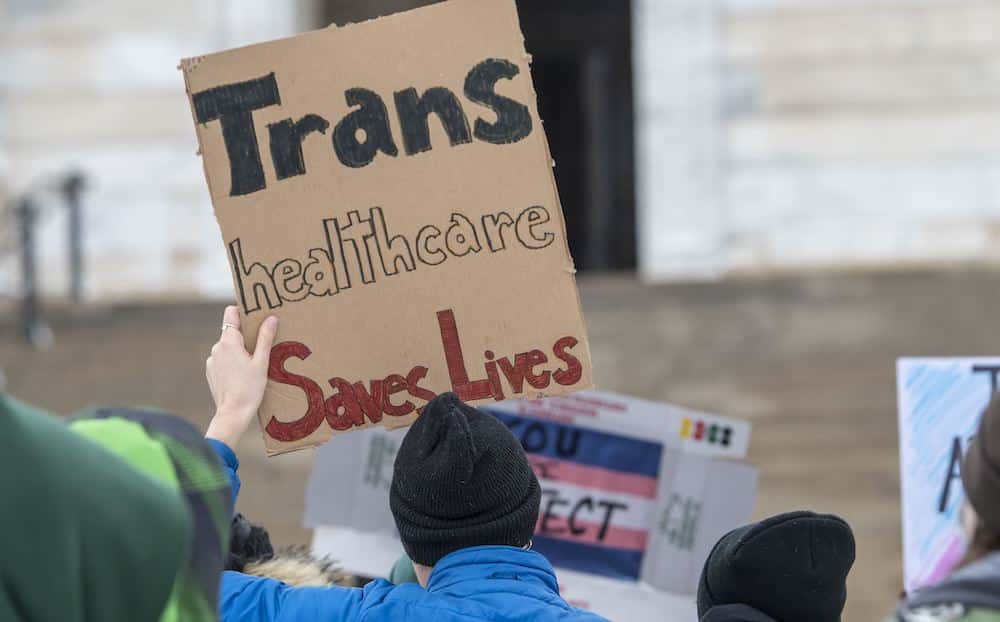Un manifestante de los derechos trans posee una señal que dice: "Trans Healthcare salva vidas".