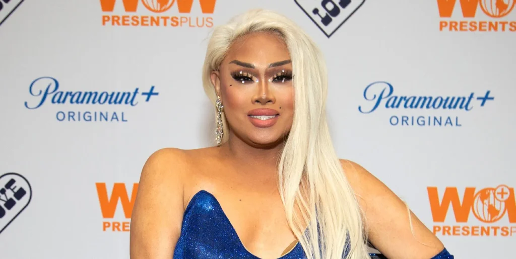 Jiggly Caliente in blonde hair and a blue dress smiling at a red carpet event in 2022.