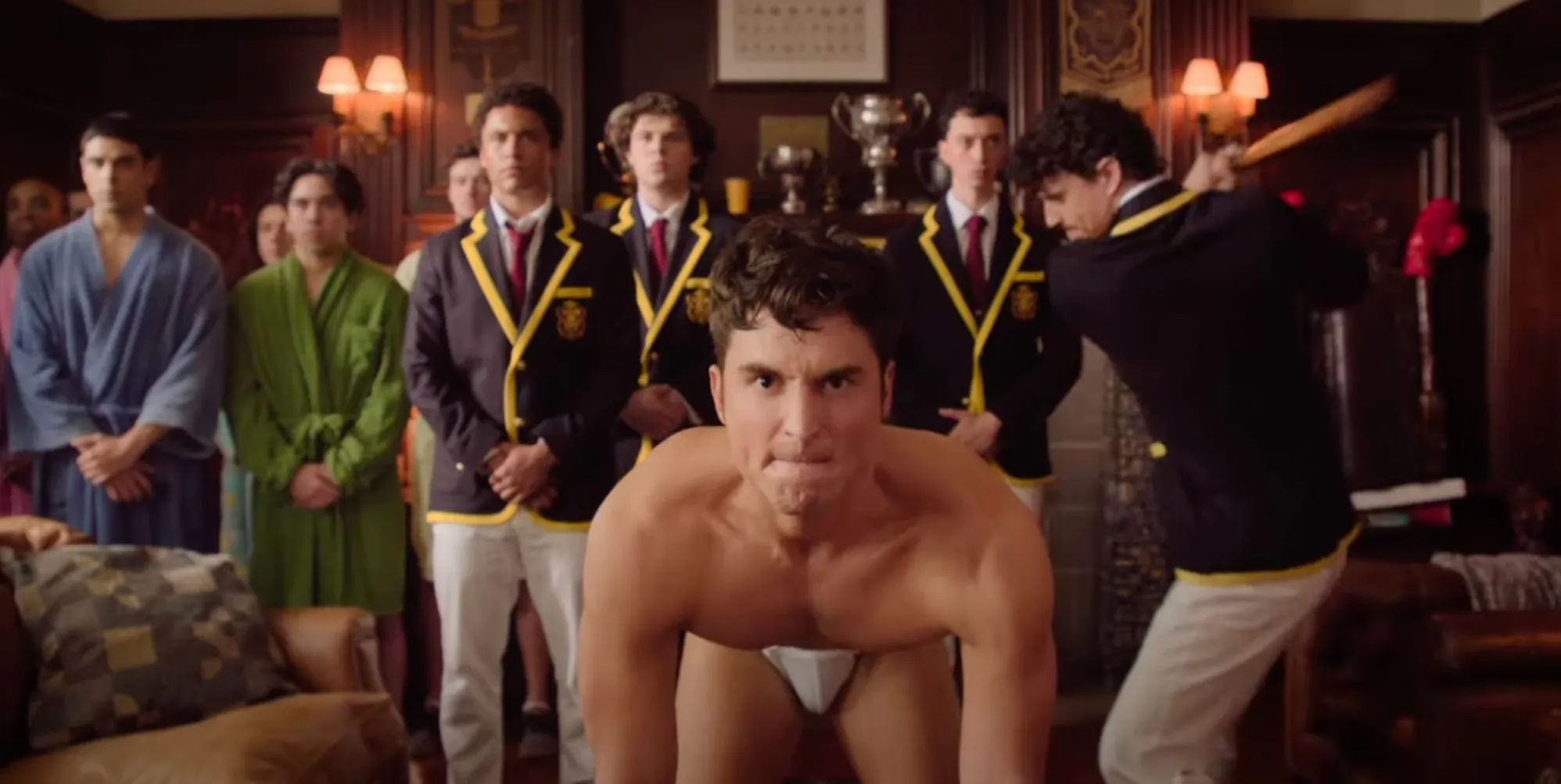 A still from Overcompensating featuring Benito Skinner on all fours in skimpy underwear preparing to be hit on the backside by a cricket bat held by Adam DiMarco.