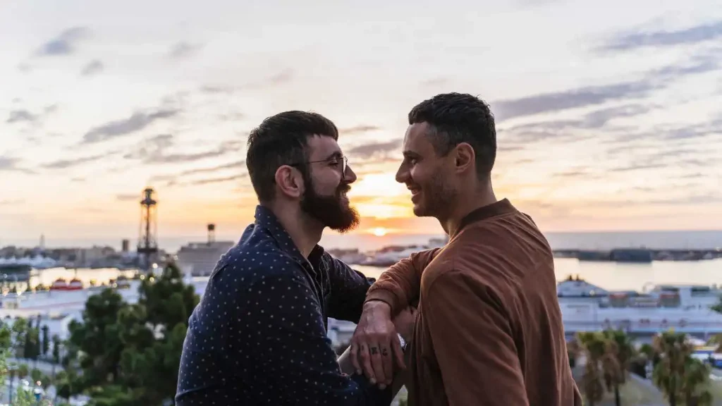 Gay couple on lookout above the city with view to the port, Barcelona, Spain.