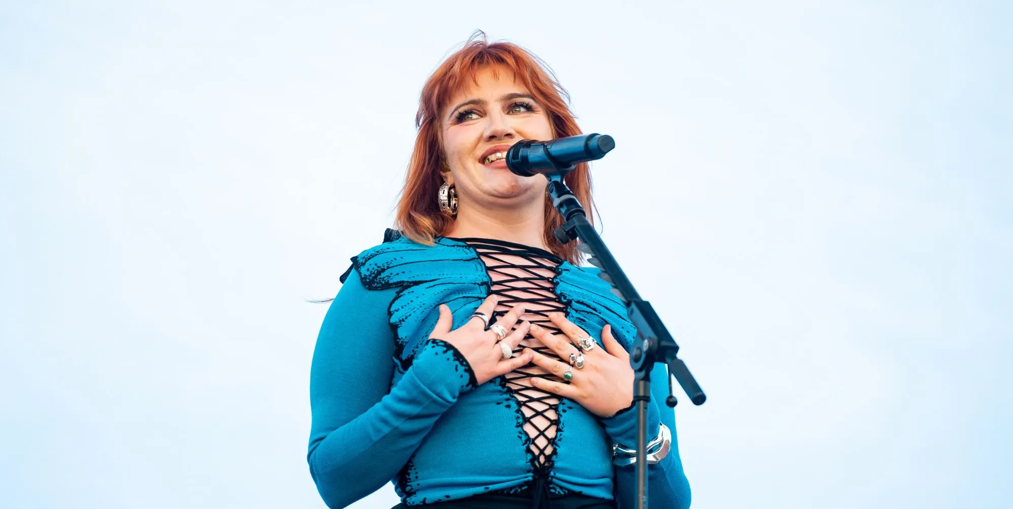CMAT performs in a blue laced up top and places her hands to her chest as she looks off to the right.