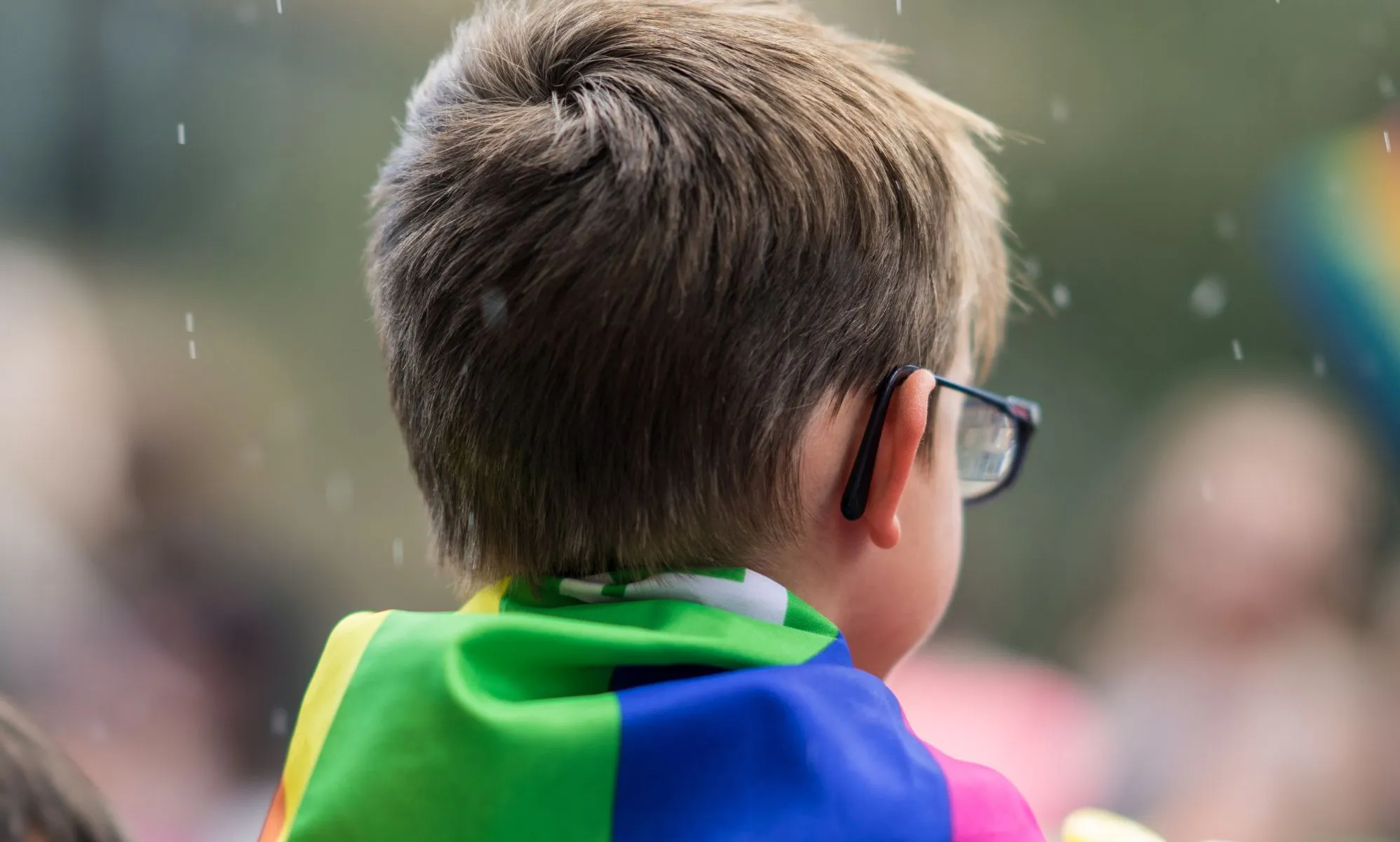 A child with a Pride flag on their shoulders.