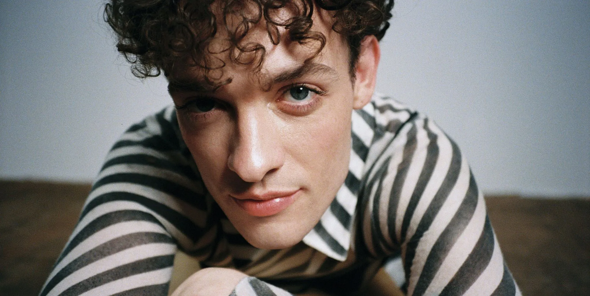 Singer Nemo smiles slightly while laying on the ground, their face close to the camera. They are wearing a striped black and white shirt.