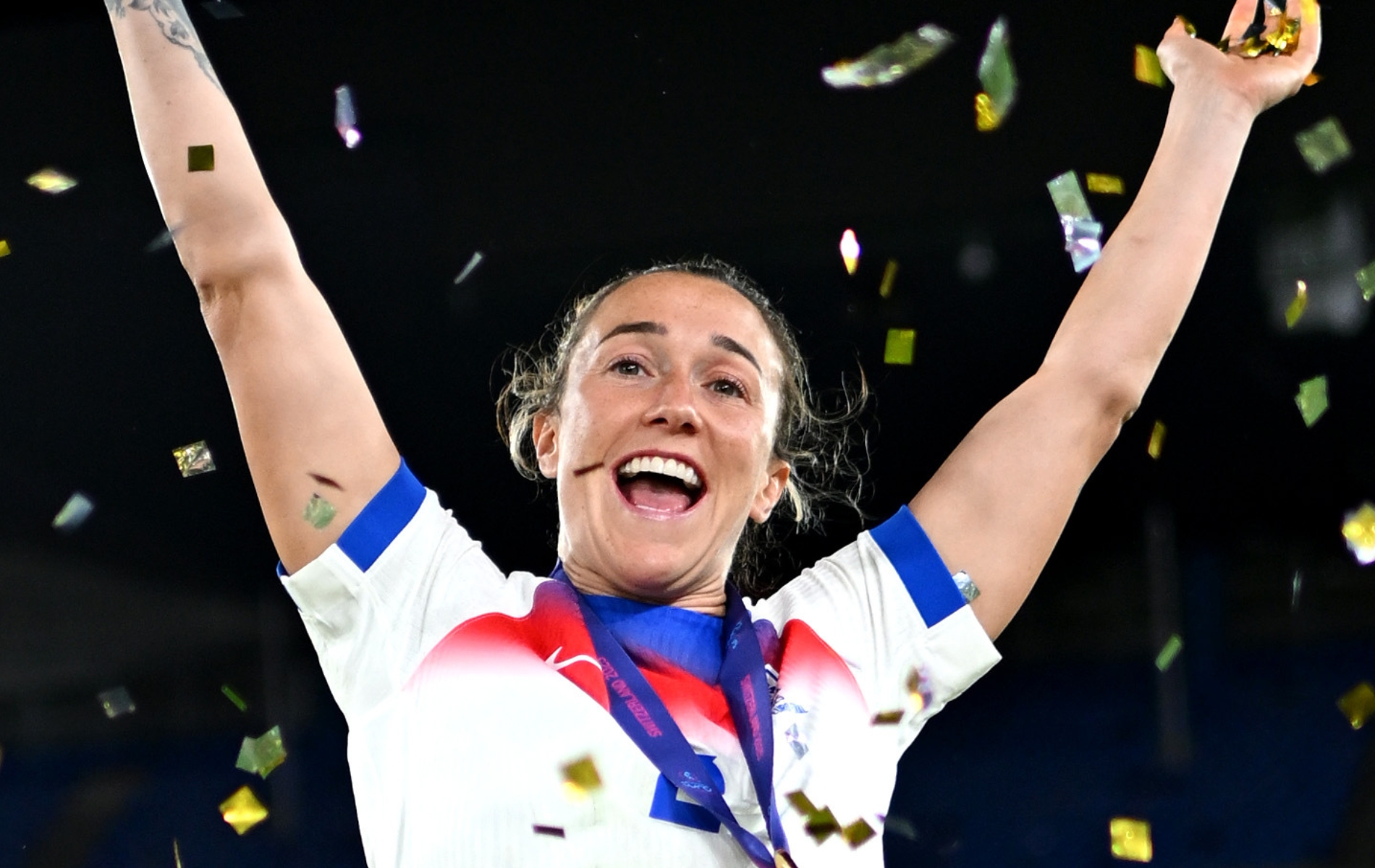 Lucy Bronze of England celebrates with her arms in the air and golden confetti around her