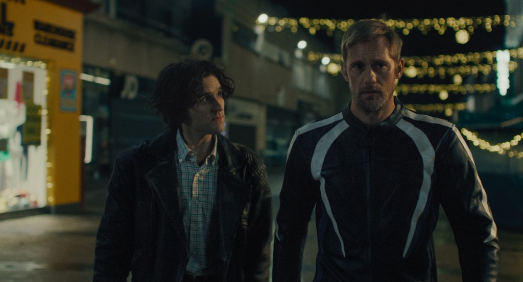 Pillion Still: Harry Melling y Alexander Skarsgård caminan juntos por la noche.
