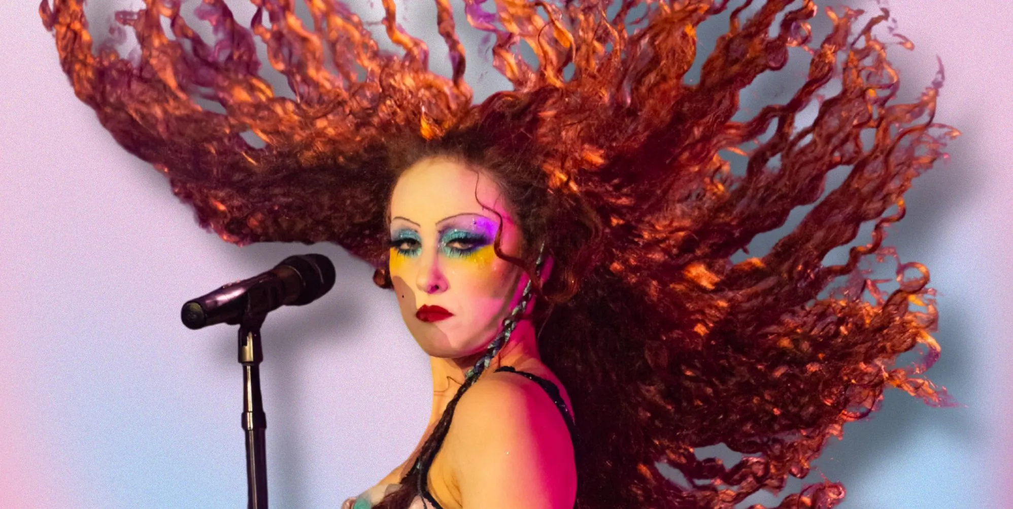 Chappell Roan stands by a microphone with her hair in the air. She is against a pink, blue and white background.