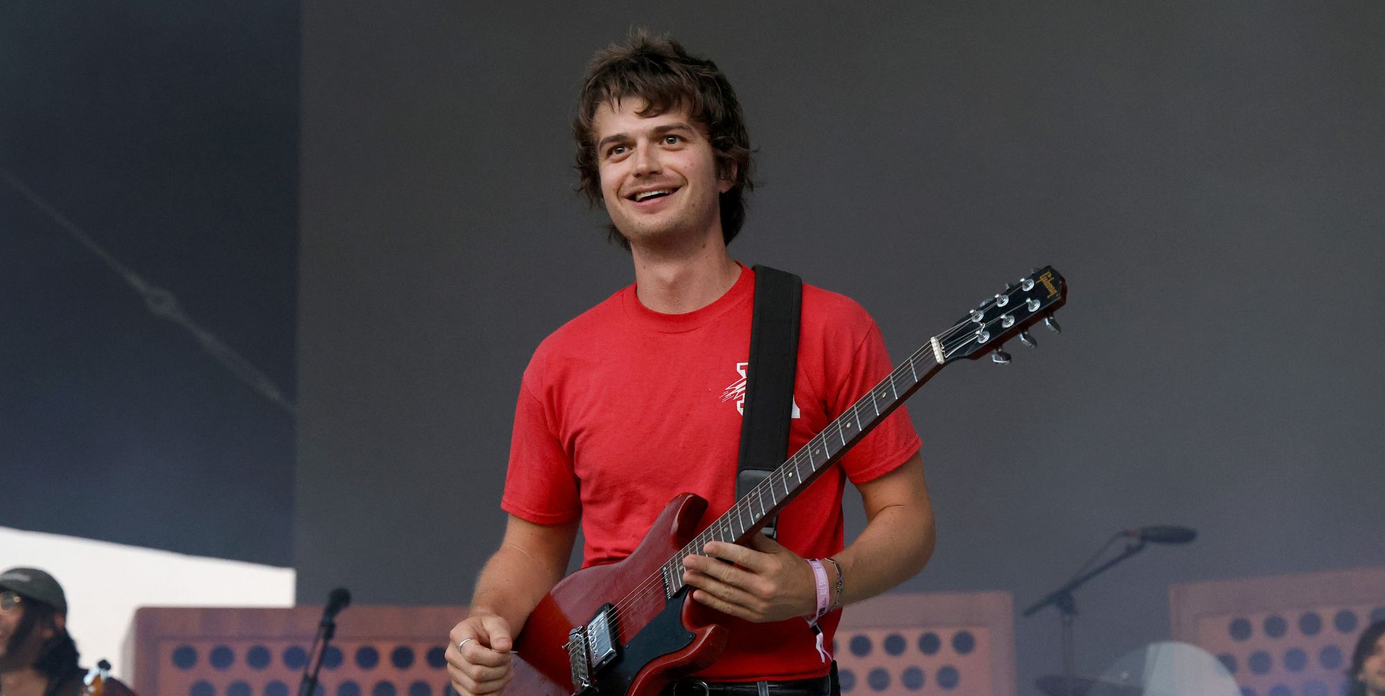 Djo performs in a red t-shirt and holds a guitar.