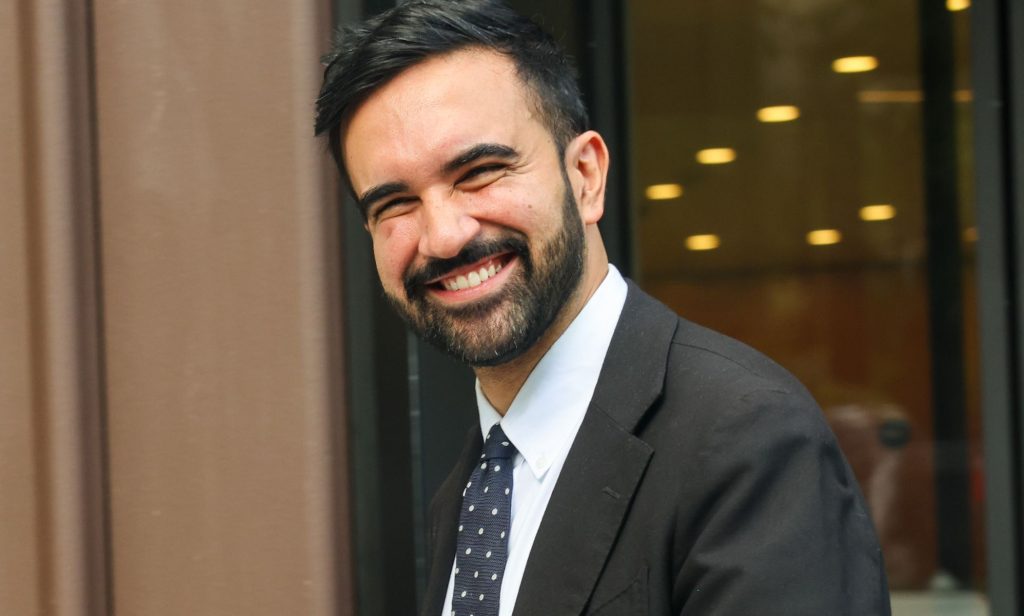 Zohran Mamdani smiling while walking through the streets of NYC.