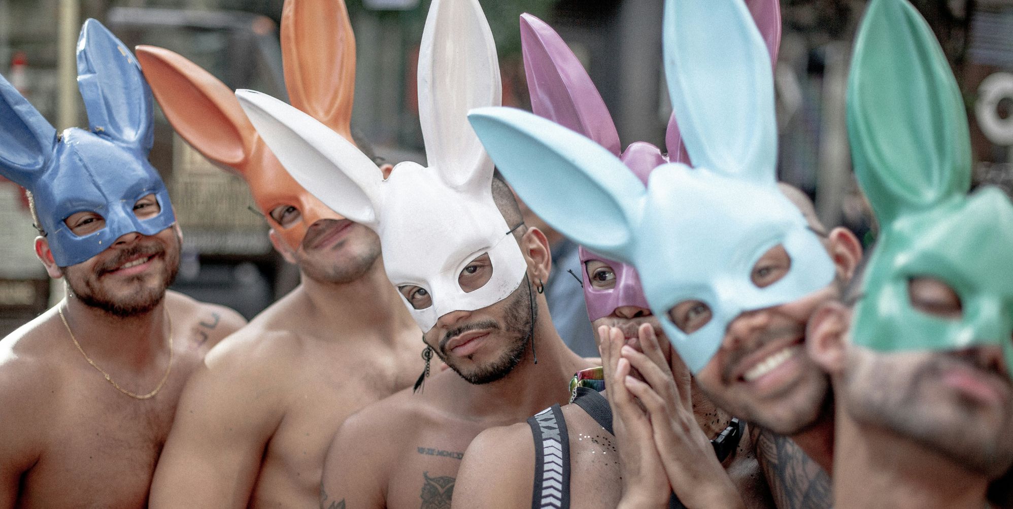 A group of shirtless men at a Pride event wearing multicoloured rabbit ears.
