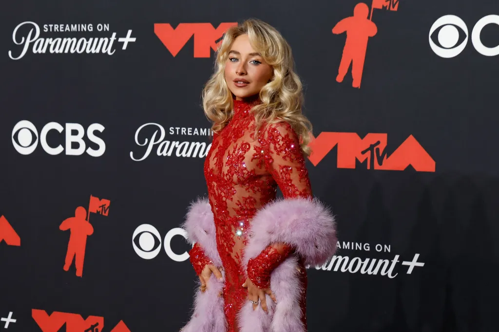 Sabrina Carpenter con un vestido rojo bordado con joyas y una esponjosa bufanda morada sobre los brazos.