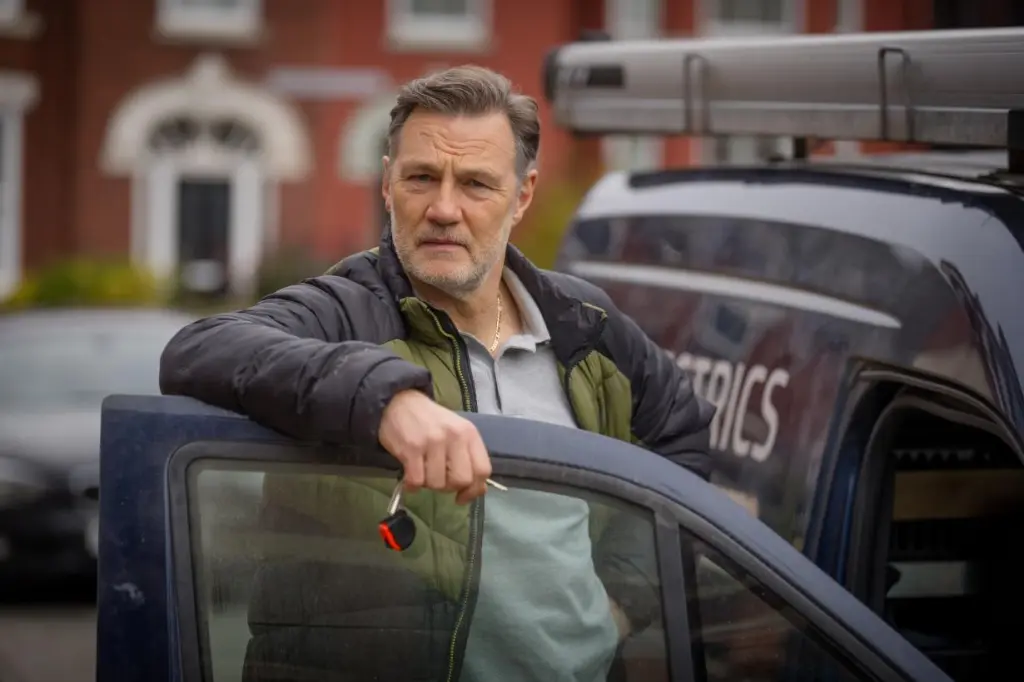 David Morrissey como Clive apoyado contra la puerta de un auto.