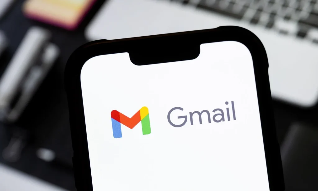 Someone holding a phone in front of a laptop with the Gmail logo visible.