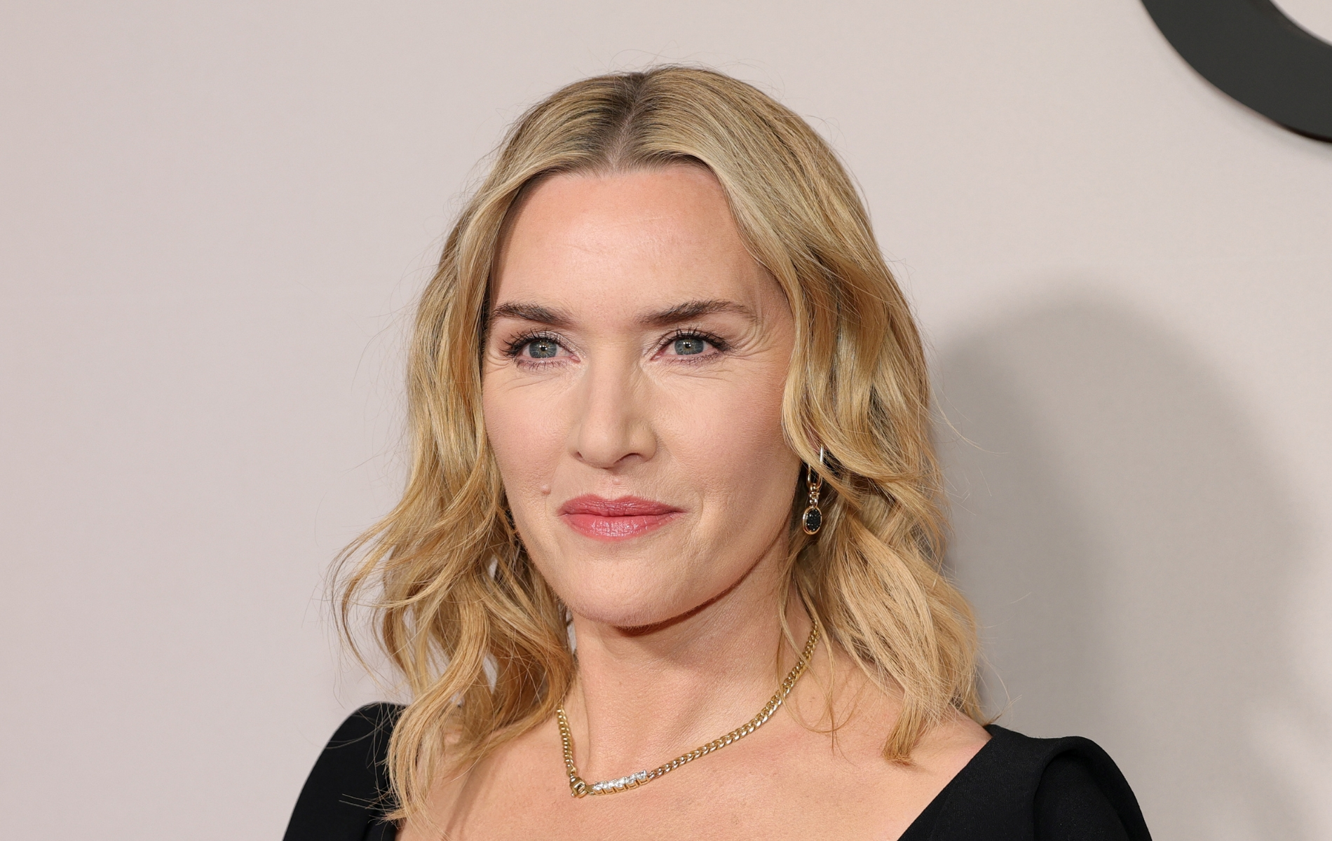 Kate Winslet looking past the camera. wearing a black top and chain necklace