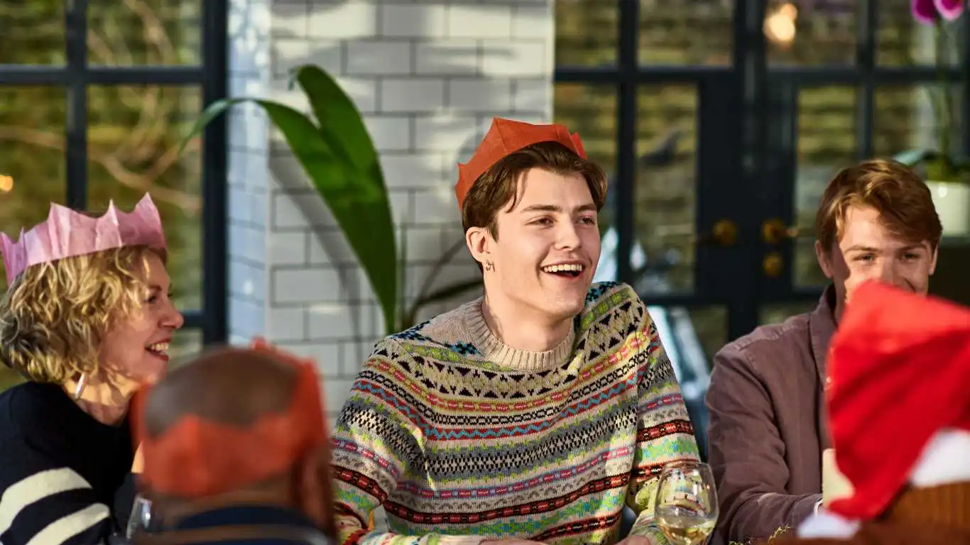 Cheerful young man wearing Christmas cracker hat playing after dinner games with family.