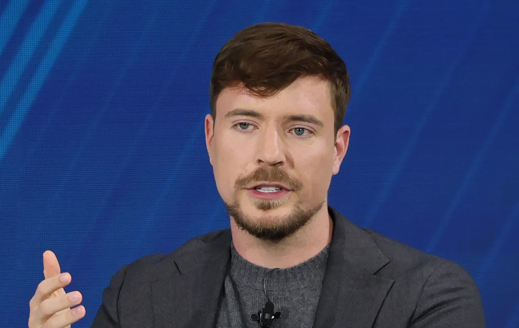 Mr Beast wearing a grey suit while speaking on a panel against a dark blue backdrop