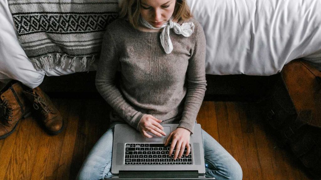 Girl sits on the floor with a laptop over her legs.