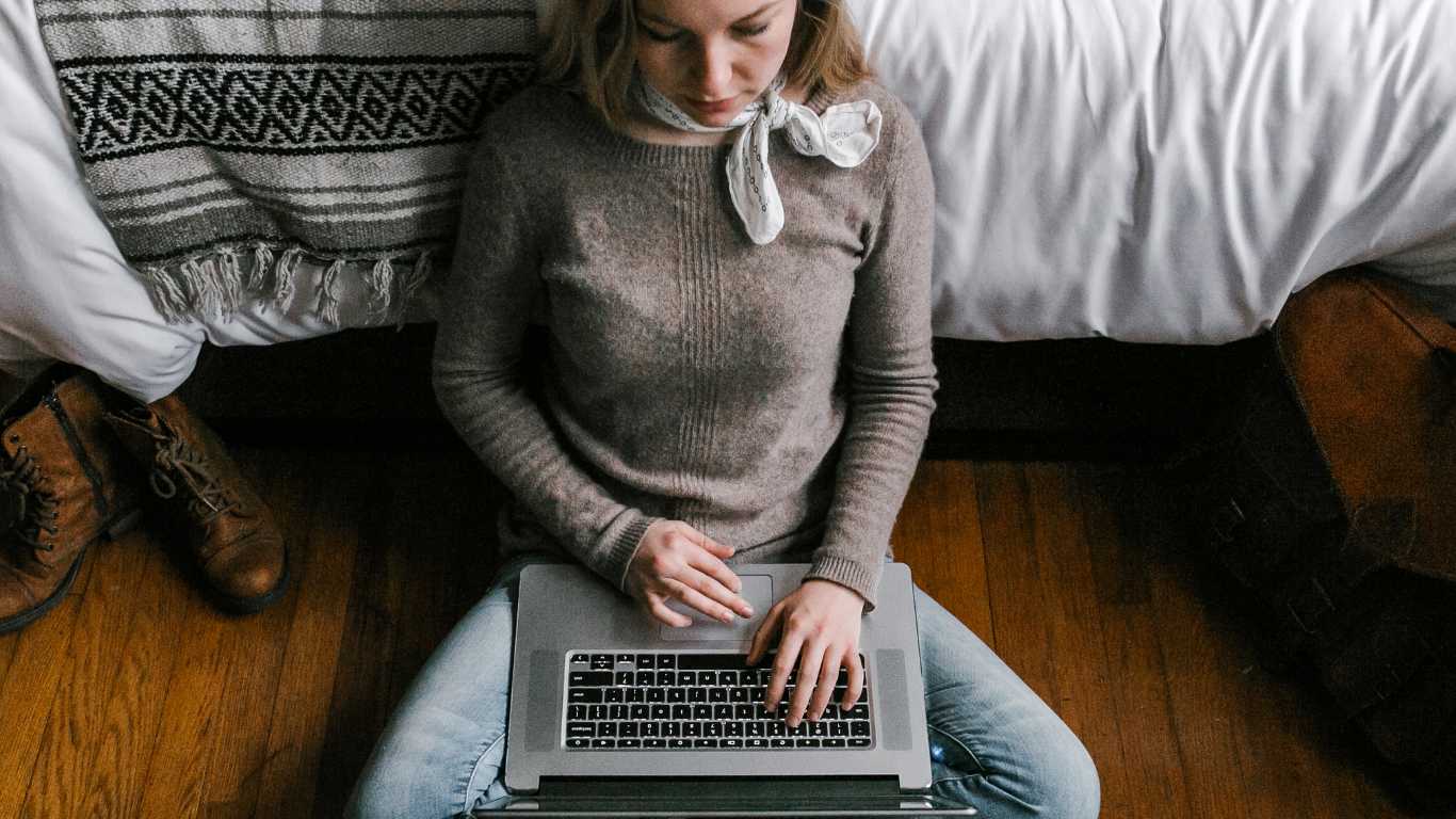 Girl sits on the floor with a laptop over her legs.