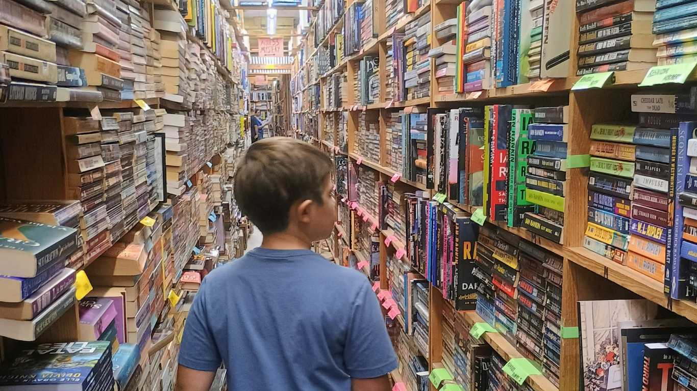 Boy walks through a library full of books.