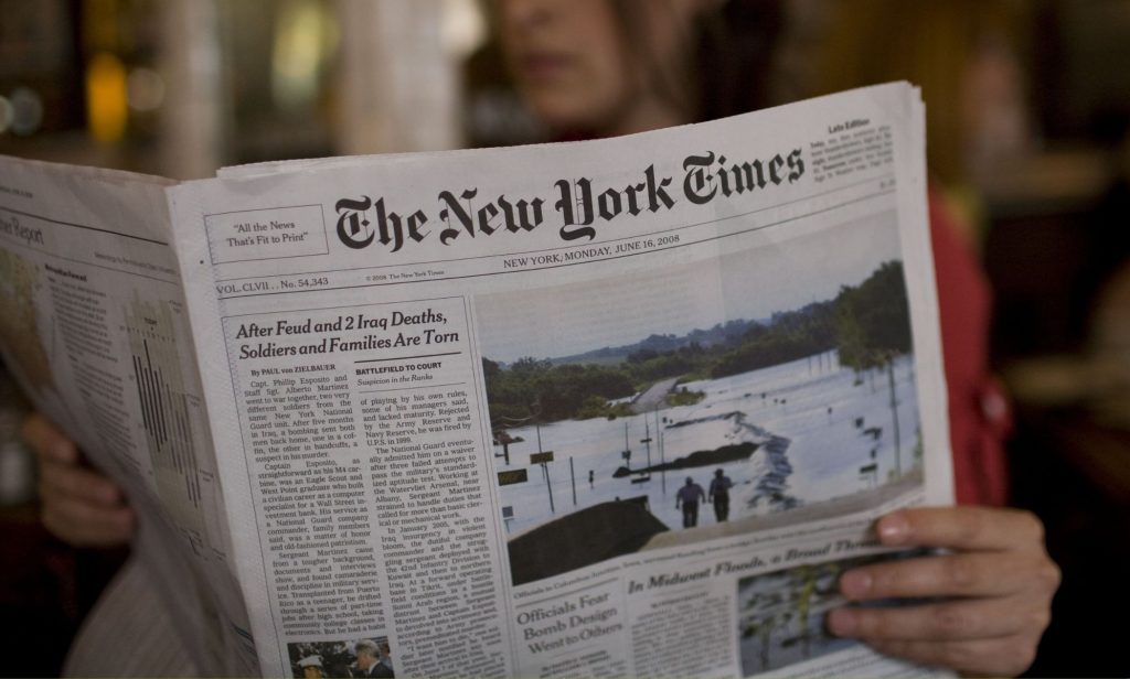 A person holding a copy of the New York Times paper.