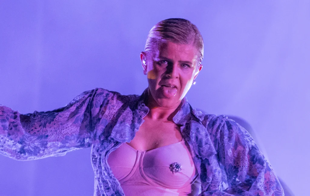 Robyn performing with a floral shirt open to reveal a bejewelled bra