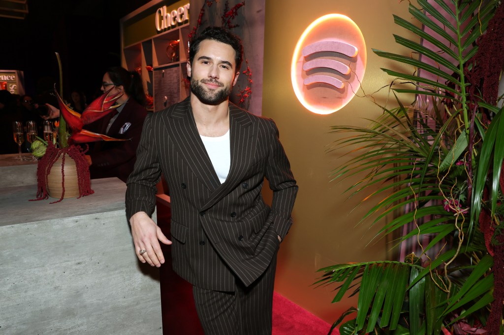 Robbie GK sonriendo con un traje a rayas marrón oscuro