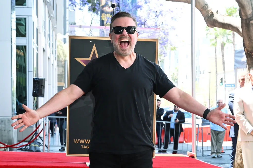 Ricky Gervais sonriendo con los brazos abiertos