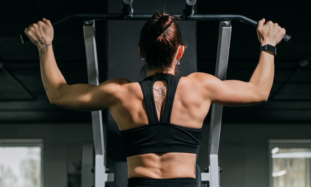A woman using a pull-up machine at the gym.