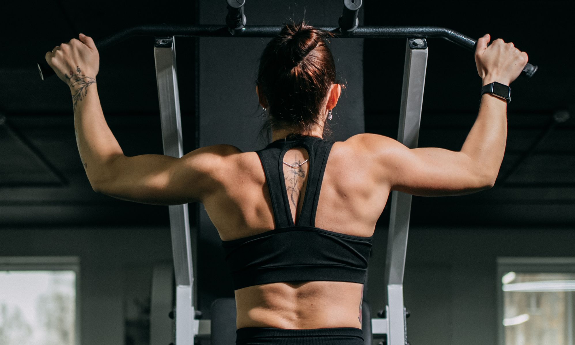 A woman using a pull-up machine at the gym.