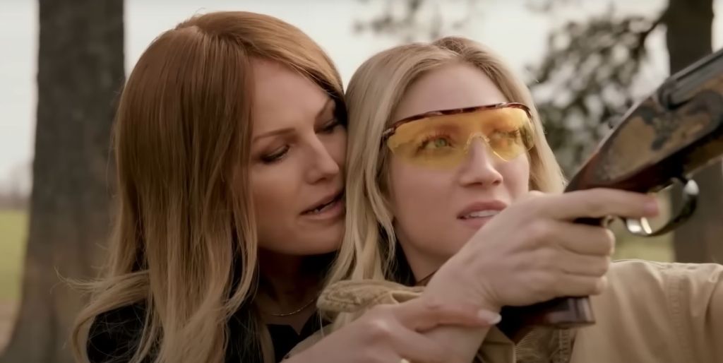 Una imagen del tráiler de Hunting Wives que muestra a Brittany Snow con gafas mientras Malin Åkerman le enseña a usar un arma.