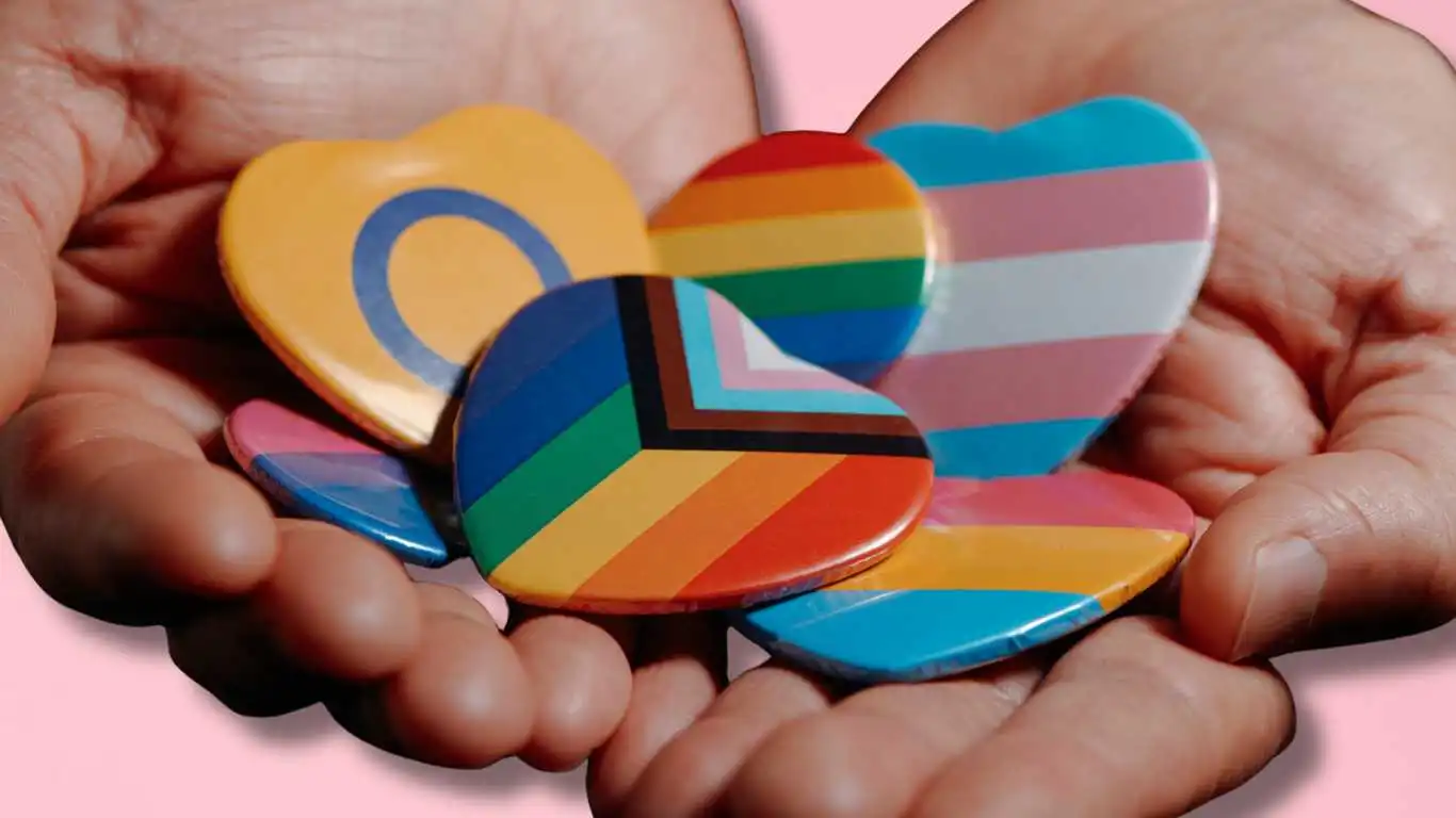 Hands held out hold LBGTQ+ badges.