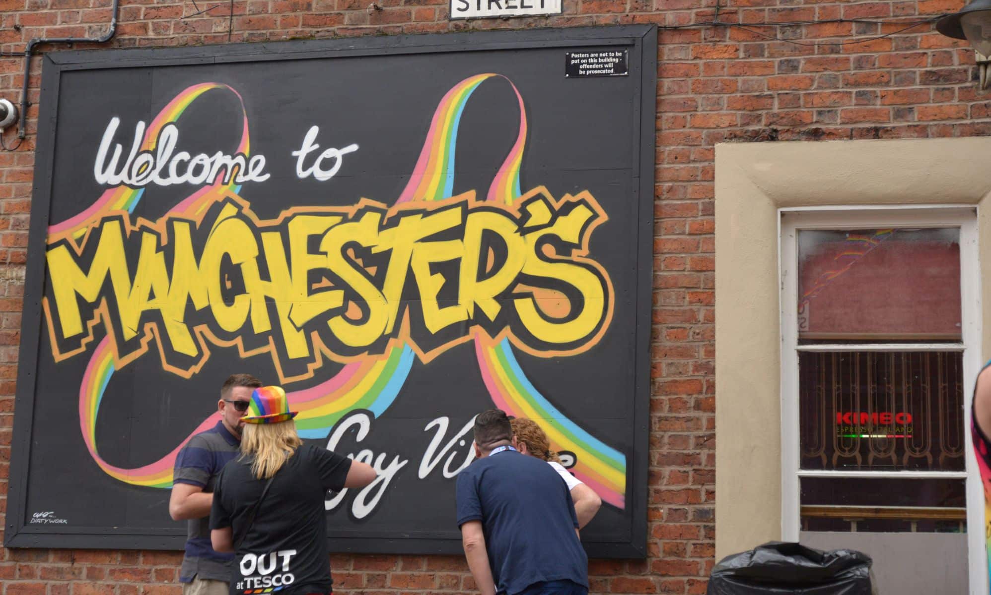 People stand next to a rainbow coloured sign for Manchester