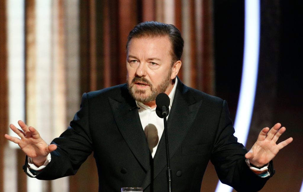 Ricky Gervais speaking into a mic with his hands up