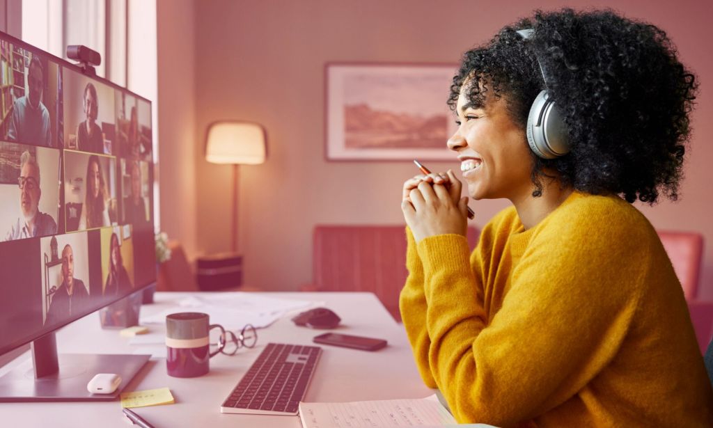 Esta es una imagen de una mujer negra sentada frente a una computadora en su casa. Ella está en una llamada de Zoom.