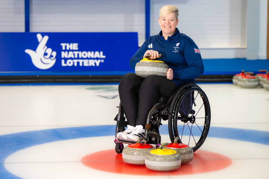 Jo Butterfield en silla de ruedas con equipo de curling en el suelo y en su regazo.