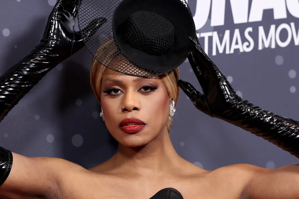 Laverne Cox con un vestido negro, guantes de cuero negros y un sombrero negro de encaje