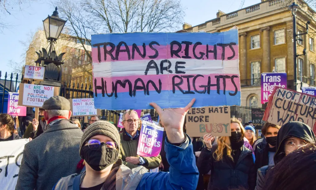 Una activista trans sostiene un cartel que dice "Los derechos trans son derechos humanos."