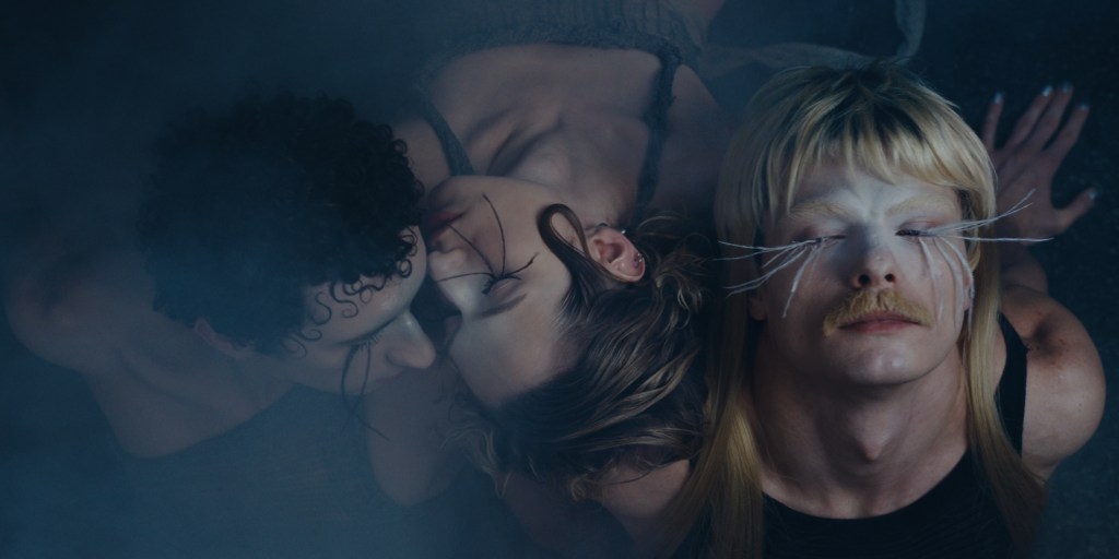 Bailar es Resistir todavía: tres bailarinas maquilladas y con pestañas larguísimas apoyando sus cabezas juntas.