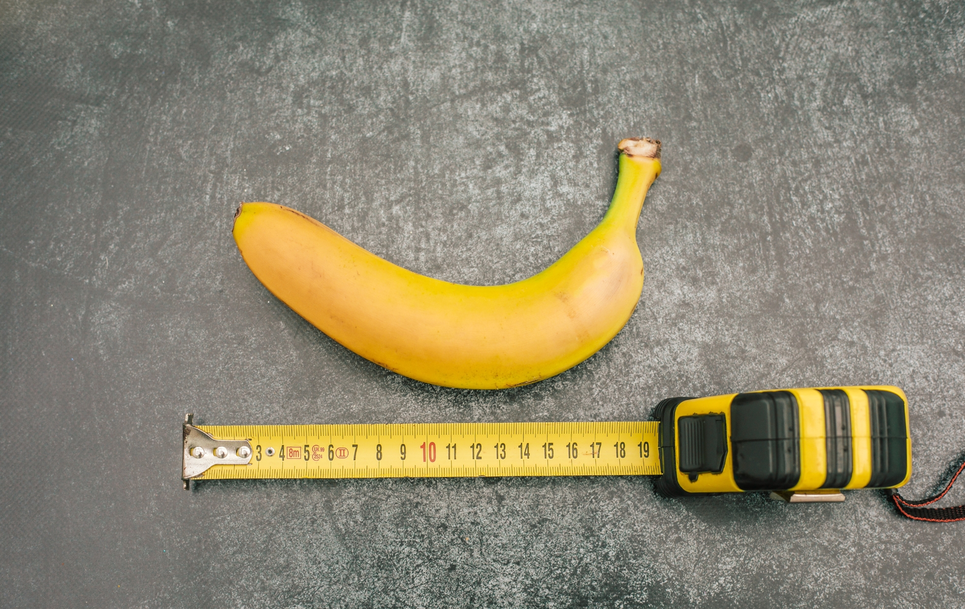banana on a grey table with a measuring tape below it