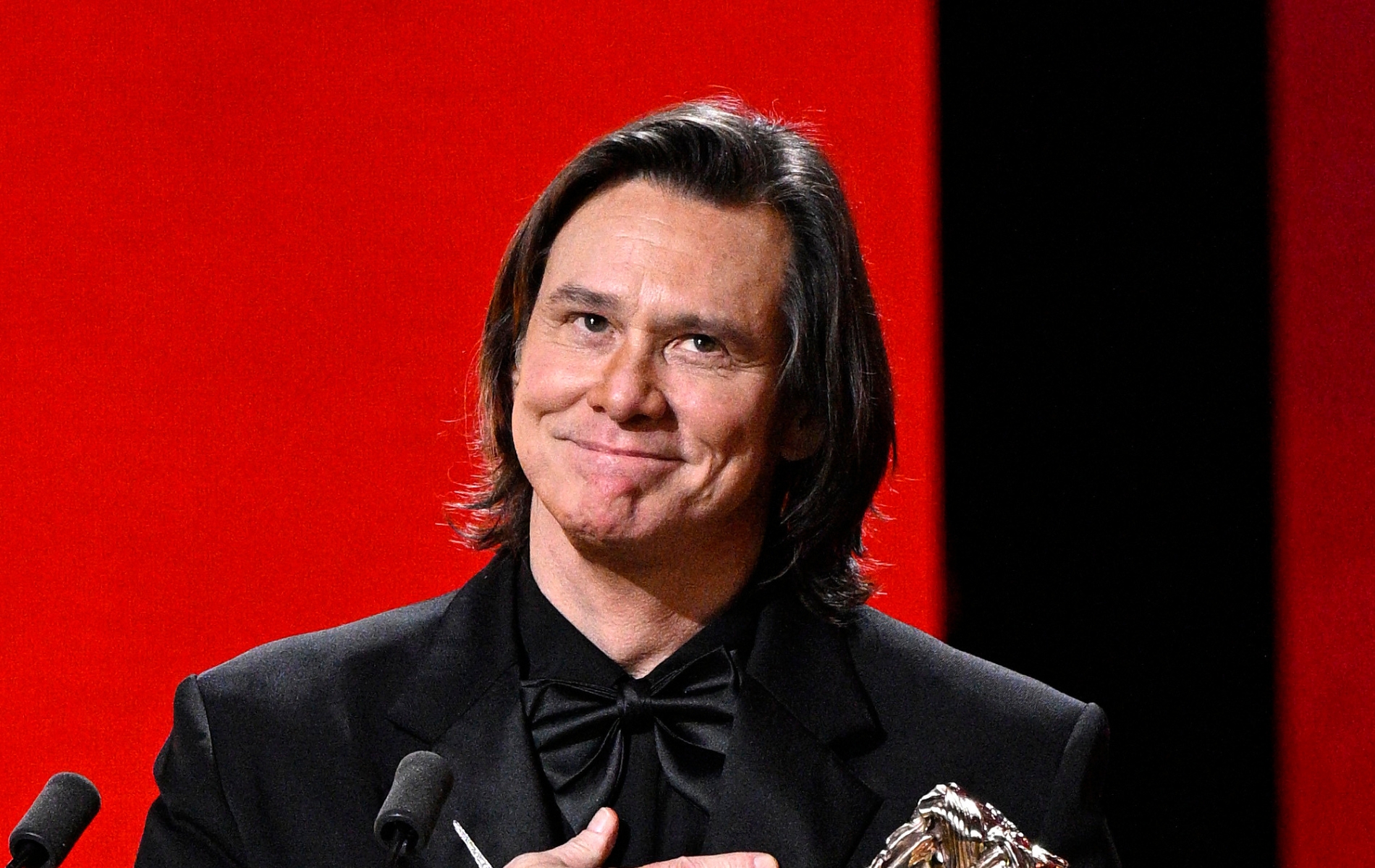 Jim Carrey in a full black suit receiving his award at the Cesar Film Awards.