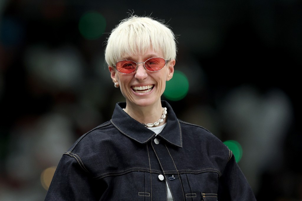 Foto en la cabeza de Megan Rapinoe, sonriendo con gafas rosas y una chaqueta vaquera oscura.