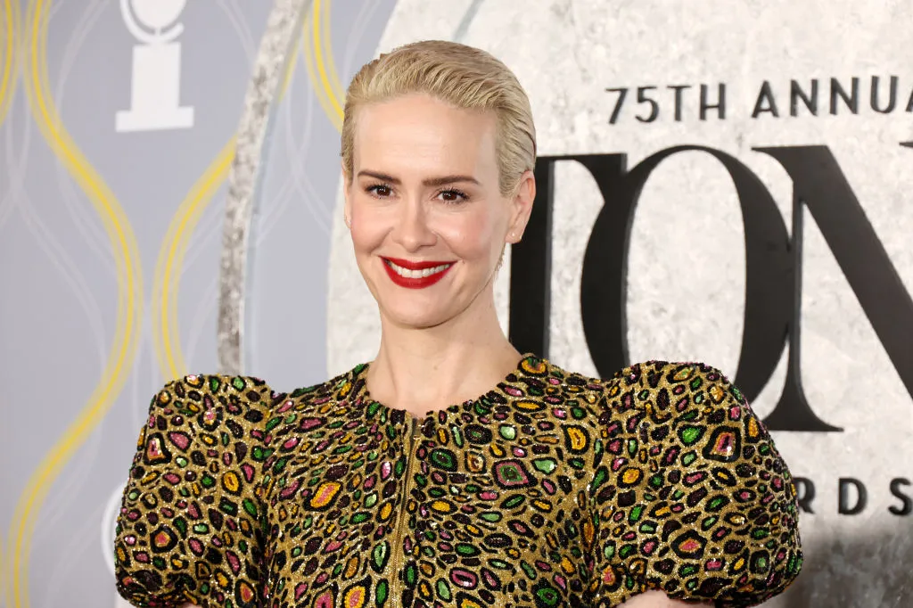 Sarah Paulson con cabello rubio corto y vestido dorado con detalles de lentejuelas metálicas.