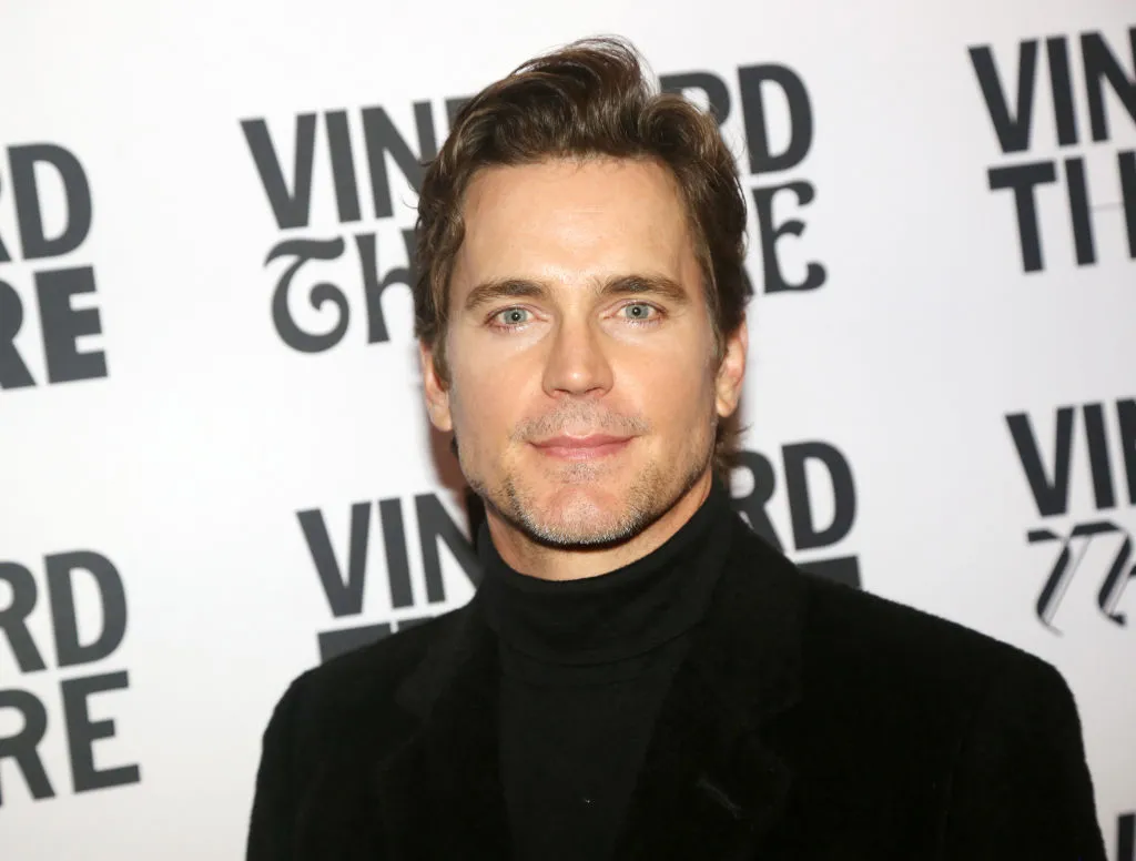 Matt Bomer con un jersey de cuello alto negro y una chaqueta negra.