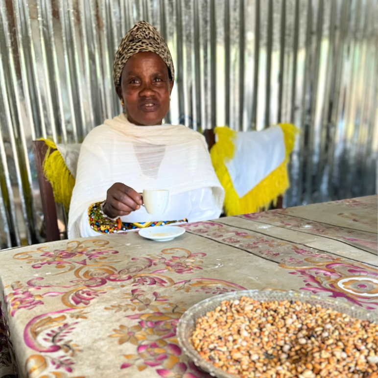 Una mujer etíope bebiendo café en una mesa con granos de café crudos en un intento frente a ella