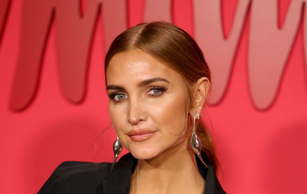 Ashlee Simpson wearing a black blazed and silver drop earrings in front of a red background