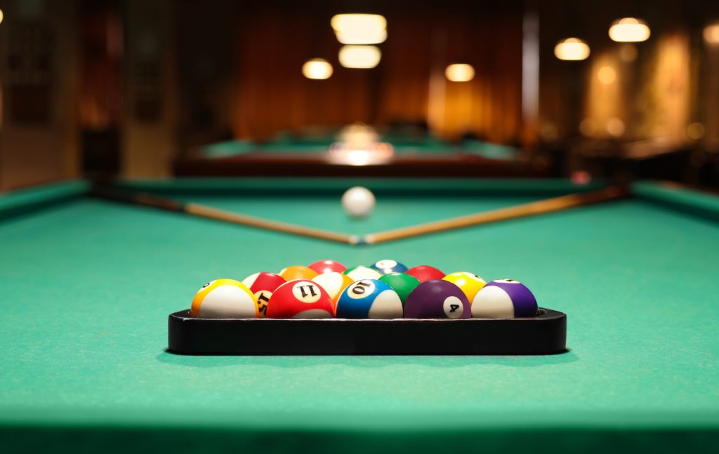 Plastic triangle rack with billiard balls and cues on green table indoors