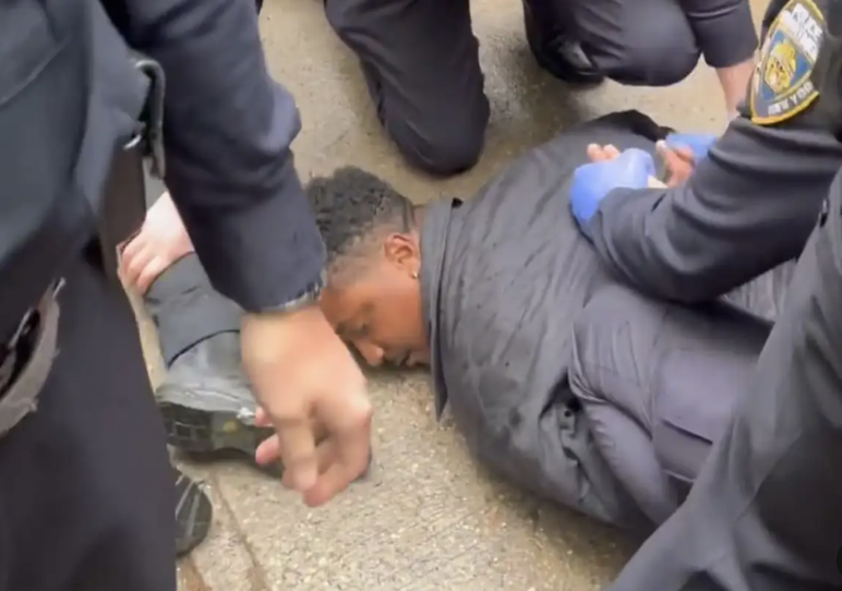 La policía esposa las manos del político negro detrás de su espalda mientras yace boca abajo en una acera mojada con un traje.